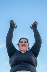 Wall Mural - Young fat woman exercising with dumbbells in the park by the lake. Healthy lifestyle