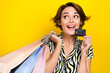 © deagreez - Portrait of excited charming woman wear striped blouse look empty space hold card shopping bags isolated on yellow color background