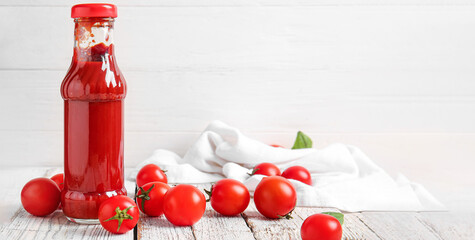 Bottle of ketchup and tomatoes on white wooden background