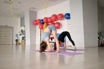 Two young Caucasian women in sportswear are doing stretching in the gym.Girls do body bends to the mat.Crab Pose.