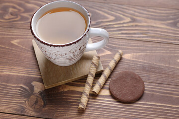 Wall Mural - Drink coaster with cup of tea, wafer rolls and cookie on wooden table