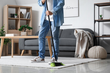 Poster - Young man sweeping carpet with broom at home