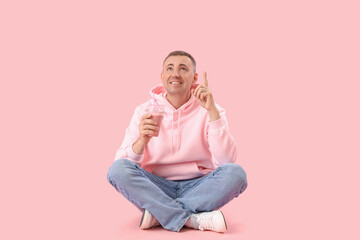 Poster - Mature man with glass of fruit smoothie pointing at something on pink background