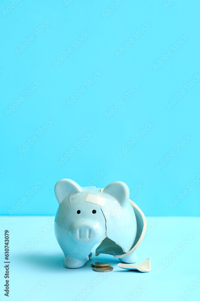 Broken patched piggy bank with money on blue background. Bankruptcy concept