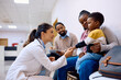© Drazen - Female pediatrician talks to black little boy who is sitting on mother's lap at clinic.