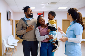 Wall Mural - Happy black family talks to nurse in hallway at doctor's office.