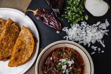 A plate of Mexican beef birria tacos of shredded beef, onions, guajillo peppers, cilantro, and broth with dipping sauce juices