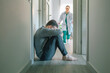 Worried female doctor running to help male patient with mental disorder and suicidal thoughts crying sitting on the floor of hallway