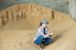 Smiling woman farmer crouched down near big pile of soybean husk for feeding livestock animals, checking quality of forage