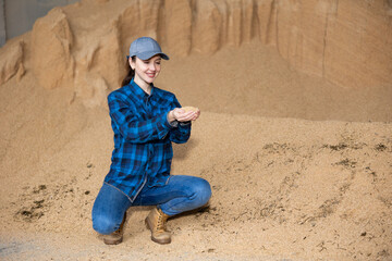 Wall Mural - Female farmer holding a handful of soybean husks in an animal feed warehouse