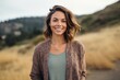 Medium shot portrait photography of a grinning woman in her 30s that is wearing a chic cardigan against a hillside or rolling hills background .  Generative AI
