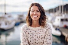Medium shot portrait photography of a grinning woman in her 30s that is wearing a cozy sweater against a bustling marina with yachts and sailboats background .  Generative AI