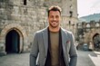 Medium shot portrait photography of a cheerful man in his 30s that is wearing a chic cardigan against a historic castle with knights and nobility background .  Generative AI