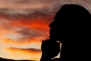 Wall Mural - Silhouette of young woman praying to God on sky background.
