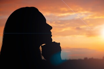Wall Mural - Silhouette of young woman praying to God on sky background.