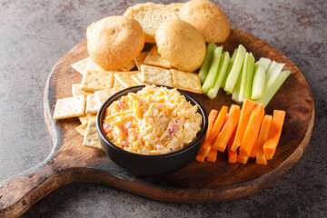 Wall Mural - Homemade Pimento Cheese Dip with carrots, celery and crackers, side view closeup on the wooden board on the table. Horizontal