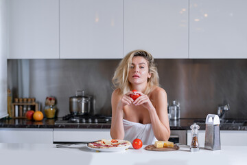 Wall Mural - Woman with ingredients for pizza, cheese, sausage and tomato. Woman eating breakfast in a kitchen. Sexy housewife on morning. Housework.