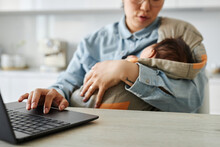 Mom Holding Her Baby And Working Online On Laptop At Table In The Kitchen
