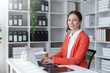 © amnaj - Charming businesswoman sitting working on laptop computer in office. Smiling female employee executive typing message using laptop computer for business in modern office.