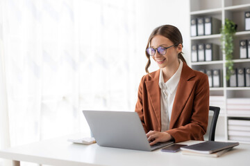 Charming businesswoman sitting working on laptop computer in office. Smiling female employee executive typing message using laptop computer for business in modern office.