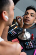 Biracial transgender man looking in mirror and putting on make-up, applying eyeshadow