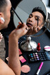 Biracial transgender man looking in mirror and putting on make-up, applying eyeshadow