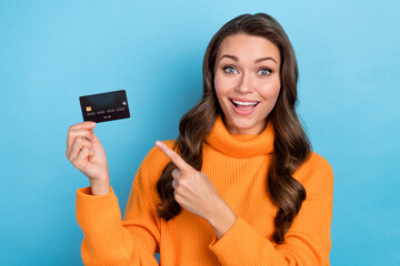 Canvas Print - Photo of positive excited woman wear orange sweater pointing finger credit card isolated blue color background