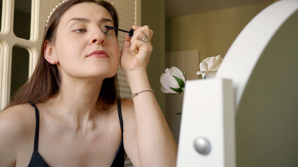 Portrait of elegant woman applying mascara at bedroom makeup table. Skin care, female health and beauty.