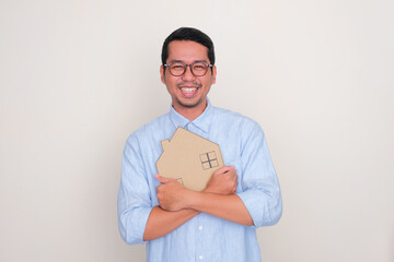 Adult Asian man smiling happy when hugging a house shape cardboard