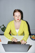 © Seventyfour - Vertical portrait of red haired young woman using laptop at workplace and smiling at camera shot with flash