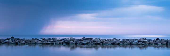 Breakwater built of stones. Long exposure photo. The Baltic Sea just before the storm.