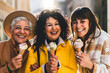Happy three mature women eating ice cream cone outdoors at city urban street-Group of senior friends having fun and enjoying fresh sweet food walking outside on sunny day-Joyful Elderly summer concept