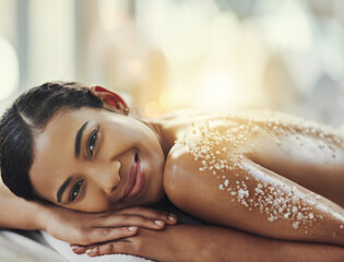 Happy woman, portrait and relax at spa in salt scrub for body treatment, skincare or massage at resort. Calm female face lying on bed in relaxation with smile for exfoliation, zen or therapy at salon