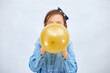 © bondarillia - Pretty little girl in casual denim dress blowing, inflate yellow balloon