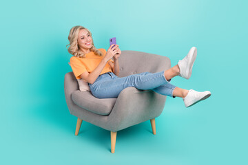 Poster - Portrait of cheerful nice person wear stylish t-shirt sit on armchair read email on smartphone isolated on turquoise color background