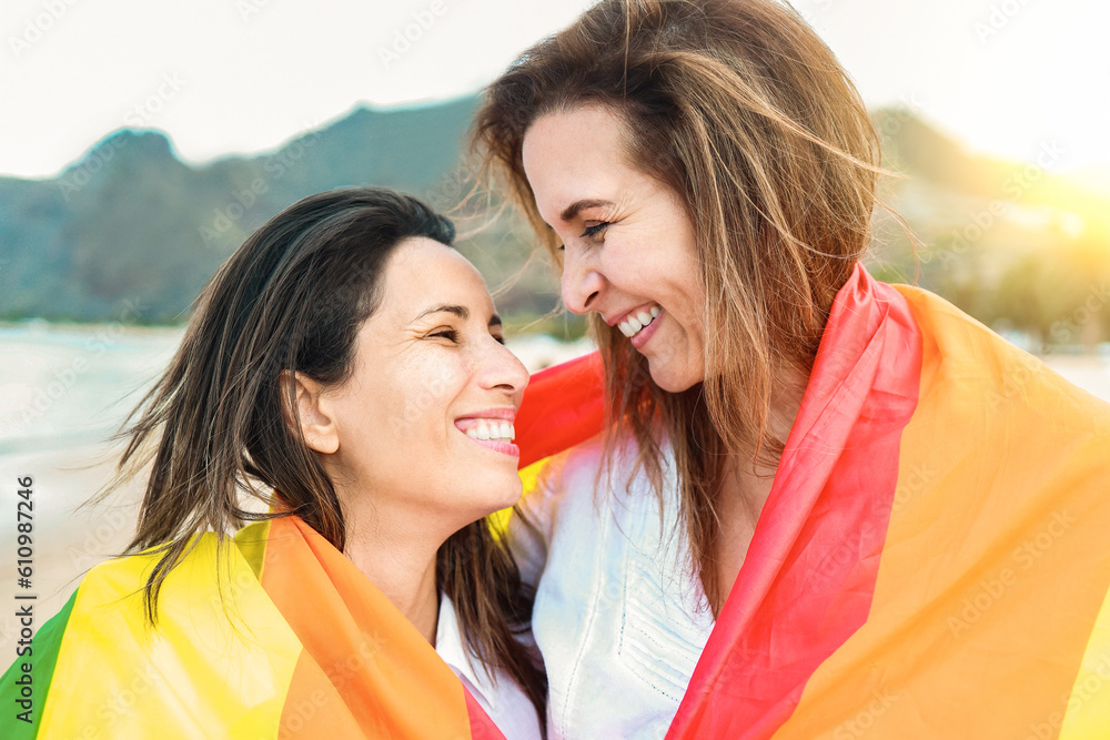 Lesbian gay couple having wearing LGBT rainbow flag with beach on ...