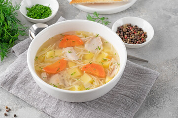 Wall Mural - Chicken soup with noodles and vegetables in white bowl on a gray concrete background.