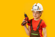 © somemeans - Portrait of boy as worker on yellow background. Child wears protective helmet and holds drill in his hand. Copy space, mock up