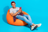Fototapeta Panele - Full body portrait of cheerful man sit comfort beanbag use smart phone telegram facebook instagram isolated on blue color background