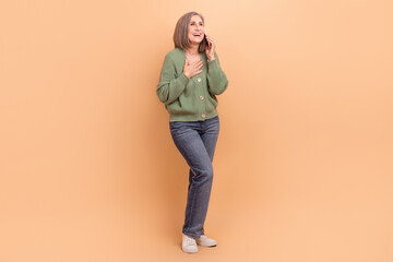 Poster - Full length photo of funny woman wear khaki cardigan arm on chest talk on smartphone look empty space isolated on beige color background