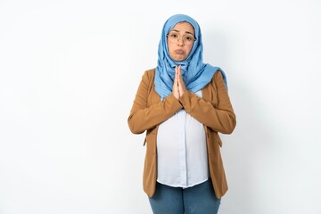 Wall Mural - Positive Young beautiful pregnant muslim woman wearing hijab over white background smiles happily, glad to receive pleasant news from interlocutor, keeps palms together, People emotions concept.