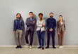 Portrait of joyful multiracial colleagues of successful business team standing in row in office. Smiling Caucasian and African American men and women in smart casual clothes posing near gray wall.