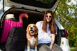 A happy girl and a beagle dog are sitting in the trunk of a car. Next to a suitcase and things for a summer vacation at sea. Traveling with a pet by car