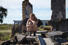 Black Angel Crying Among The Ruins Of A Building After The Apocalypse. Young, Beautiful, Blonde Woman With Black Wings And Mascara Running Down Her Face After Crying. She Is Sad And Depressed.