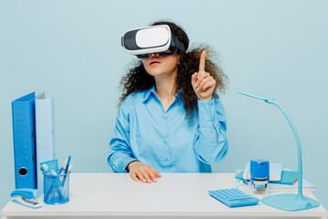 Wall Mural - Young successful employee business woman in casual shirt sit work at white office desk watching in vr headset pc gadget raise up finger isolated on plain pastel light blue background studio portrait