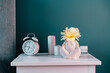 © okrasiuk - Closeup white bedside table with clock, female body-shaped vase with rose flower and candles on turquoise wall background. Modern stylish female bedroom. Self recovery place at home. Selective focus.