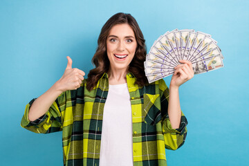 Sticker - Portrait of excited charming lady demonstrate thumb up approval hold dollar bills isolated on blue color background