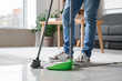 © Pixel-Shot - Young man sweeping floor with broom at home