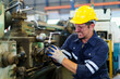 © DG PhotoStock - Professional caucasian white ethnicity male technician operating the heavy duty machine in the lathing factory. Technician in safety and helmet suit controlling a machine in factory.