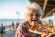 © Markus Schröder - Headshot portrait photography of a glad old woman eating a piece of pizza against a scenic beach pier background. With generative AI technology
